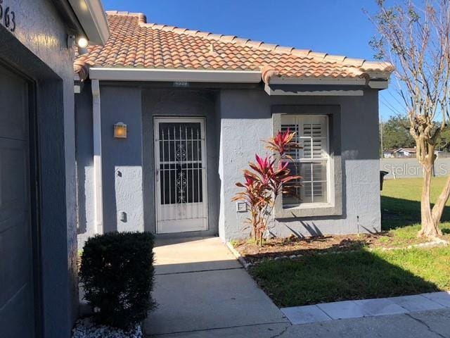 view of exterior entry with a lawn, a tile roof, and stucco siding