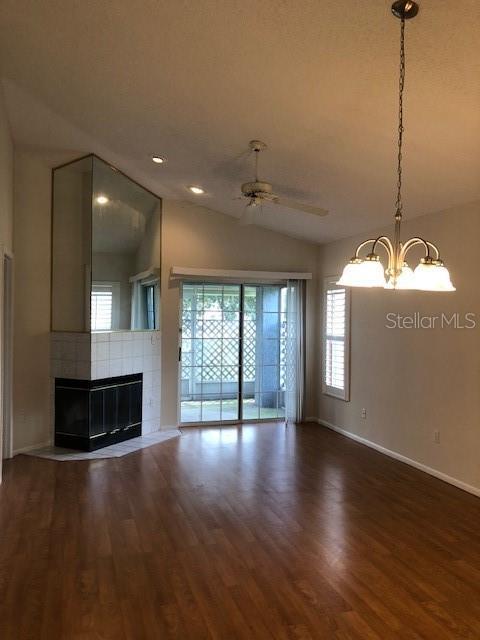 unfurnished living room featuring lofted ceiling, ceiling fan with notable chandelier, dark hardwood / wood-style flooring, and a tile fireplace