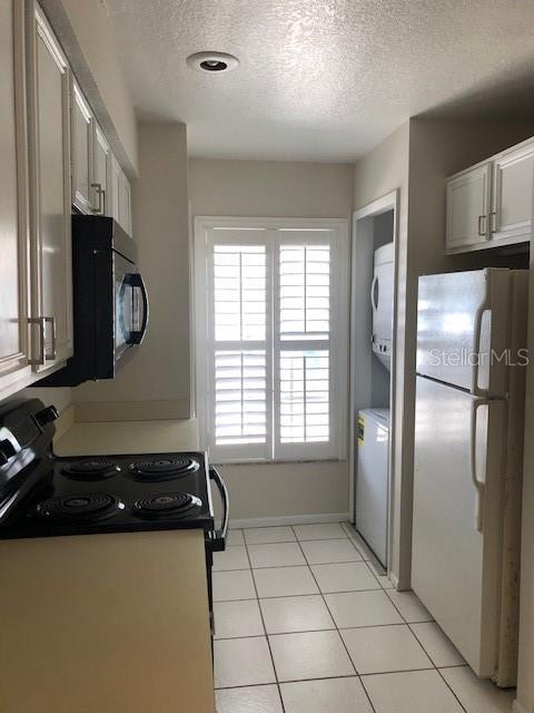 kitchen featuring white cabinets, stacked washer / drying machine, white refrigerator, and light tile patterned floors