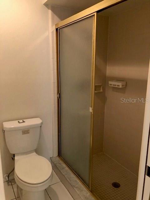 bathroom with a shower with shower door, toilet, and tile patterned floors