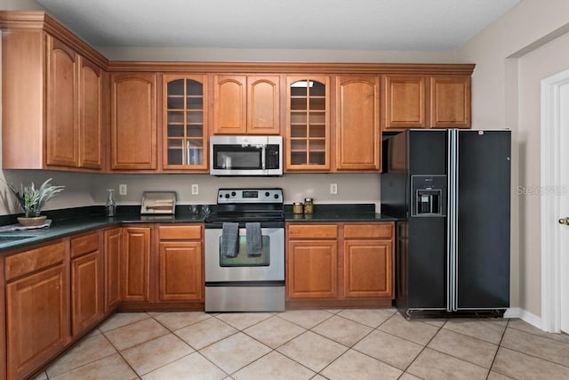 10617 Bamboo Rod Cir, Riverview, FL 33569 - kitchen with stainless steel appliances, dark countertops, brown cabinetry, glass insert cabinets, and light tile patterned floors