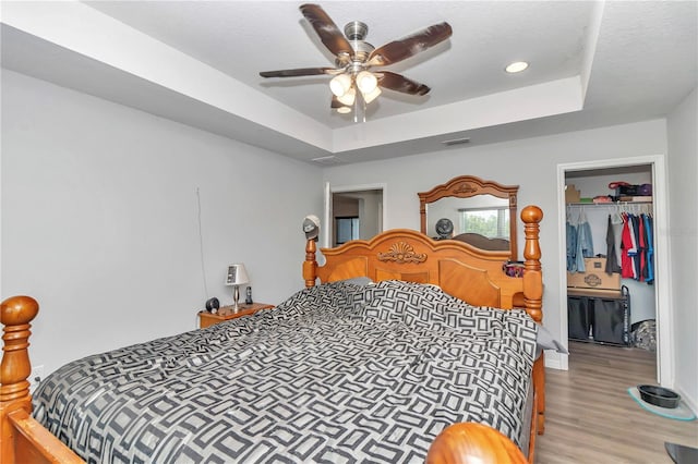 bedroom with hardwood / wood-style flooring, a closet, ceiling fan, and a tray ceiling