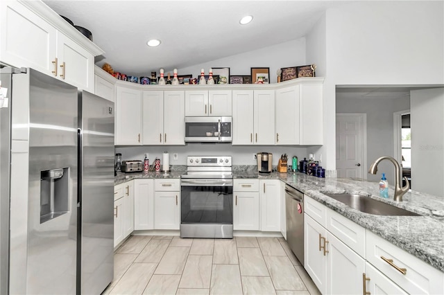 kitchen featuring vaulted ceiling, light stone counters, stainless steel appliances, white cabinetry, and sink