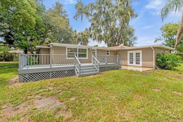 back of property with stucco siding, a deck, a lawn, and french doors