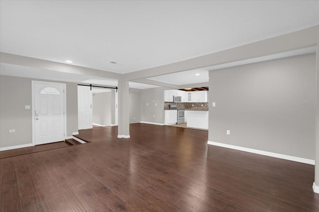 unfurnished living room featuring wood finished floors, baseboards, and a barn door