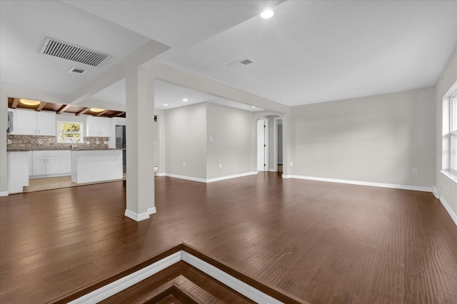 unfurnished living room featuring arched walkways, visible vents, baseboards, and wood finished floors