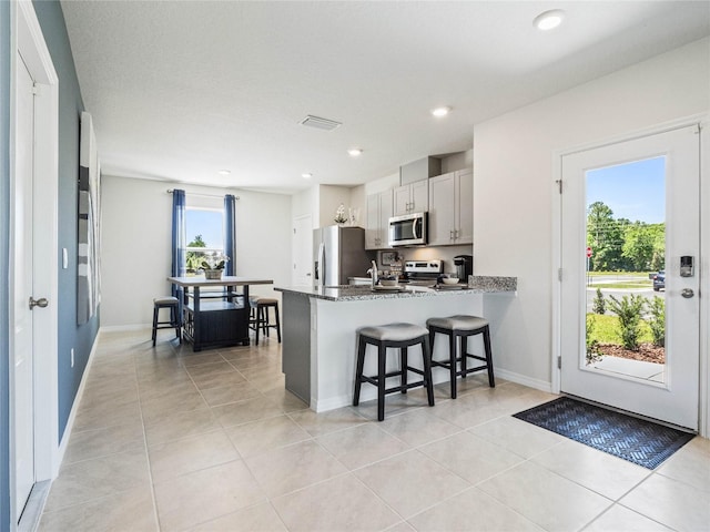 kitchen with stainless steel appliances, a peninsula, a kitchen breakfast bar, white cabinets, and dark stone countertops