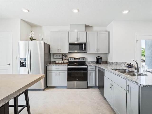 kitchen featuring light stone counters, stainless steel appliances, gray cabinetry, a sink, and light tile patterned flooring