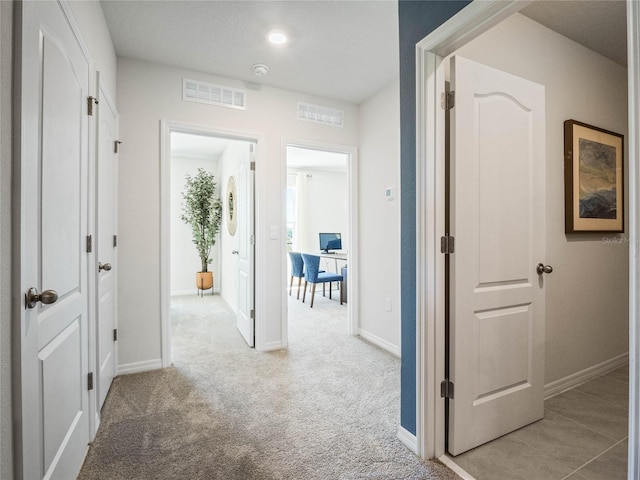 hall featuring baseboards, visible vents, and light colored carpet