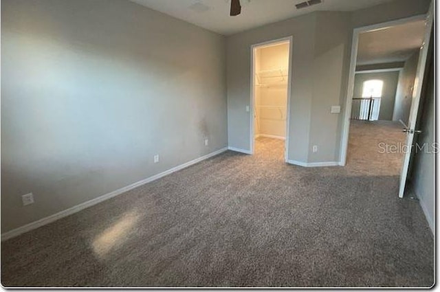 unfurnished bedroom featuring a walk in closet, ceiling fan, a closet, and carpet floors