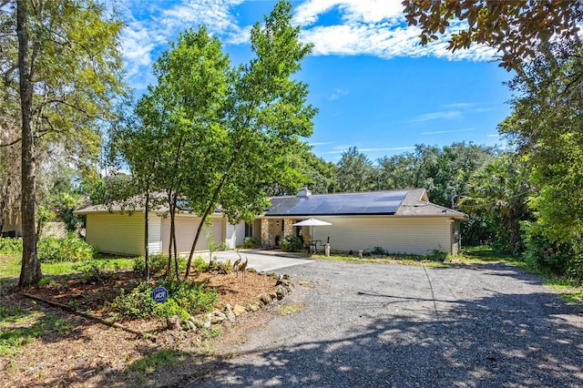 view of front facade with an attached garage, gravel driveway, and roof mounted solar panels