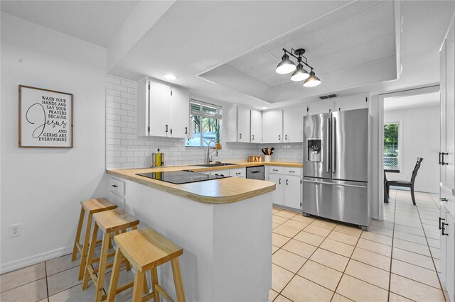 kitchen featuring backsplash, a raised ceiling, white cabinetry, a breakfast bar area, and stainless steel appliances