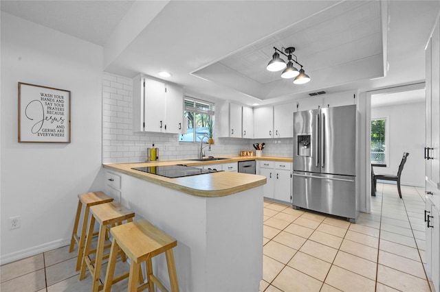 kitchen featuring a tray ceiling, stainless steel refrigerator with ice dispenser, light countertops, decorative backsplash, and light tile patterned flooring