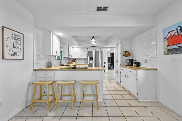 kitchen featuring white cabinets, stainless steel refrigerator with ice dispenser, sink, kitchen peninsula, and a breakfast bar area