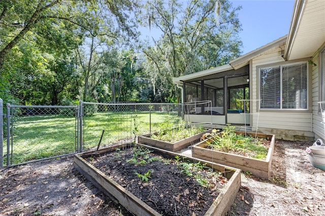 view of yard featuring a sunroom, a gate, fence, and a garden