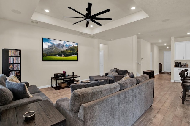 living room featuring a tray ceiling, ceiling fan, and light wood-type flooring