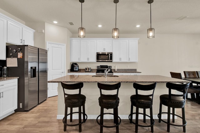 kitchen with stainless steel appliances, a kitchen island with sink, dark stone counters, and light hardwood / wood-style floors