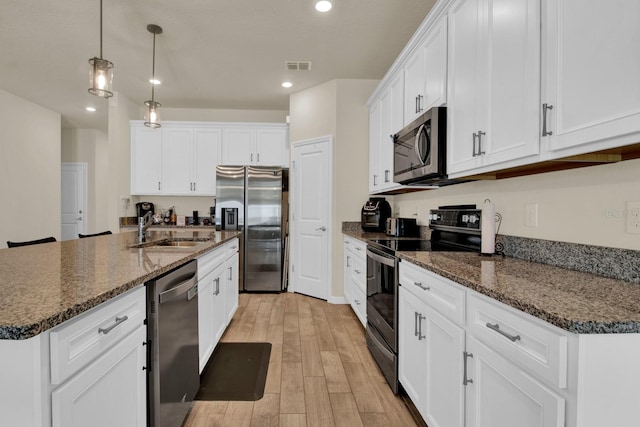 kitchen with white cabinets, light hardwood / wood-style flooring, dark stone countertops, an island with sink, and appliances with stainless steel finishes