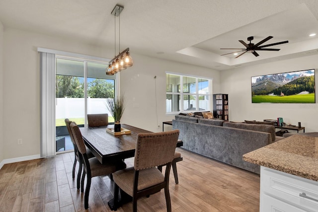 dining room with ceiling fan, a textured ceiling, a tray ceiling, and light hardwood / wood-style flooring