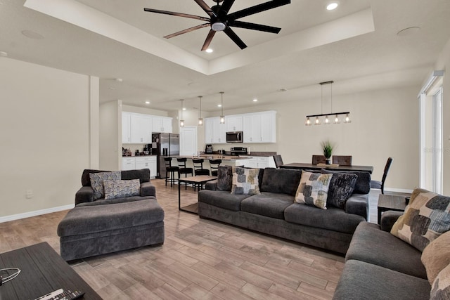 living room with a raised ceiling, ceiling fan, and light wood-type flooring