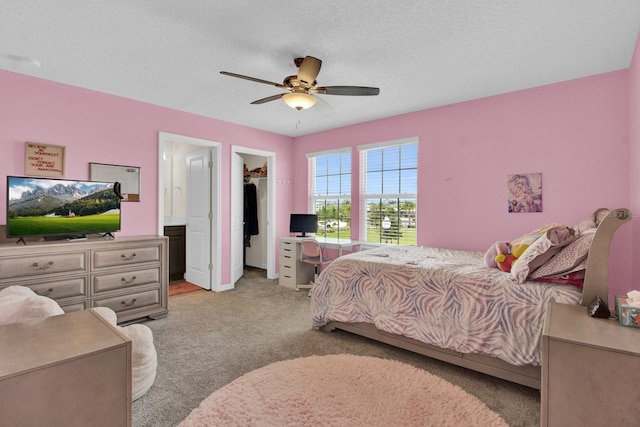 bedroom featuring connected bathroom, ceiling fan, light colored carpet, a textured ceiling, and a walk in closet