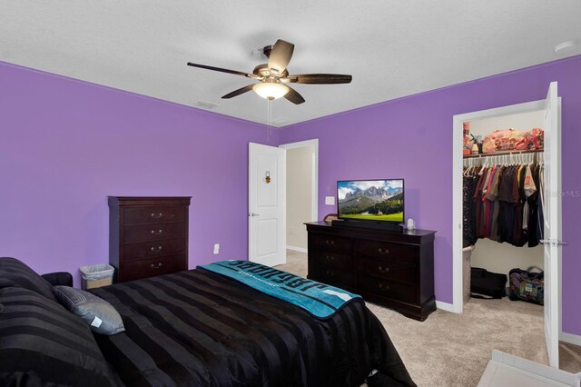 bedroom featuring light carpet, a walk in closet, a closet, and ceiling fan