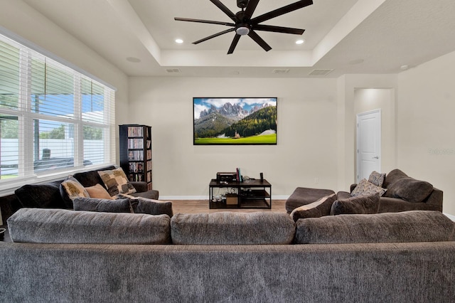 living room with hardwood / wood-style floors, a raised ceiling, and ceiling fan