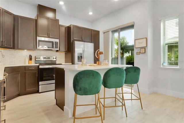 kitchen with appliances with stainless steel finishes, a healthy amount of sunlight, a kitchen island with sink, and dark brown cabinetry