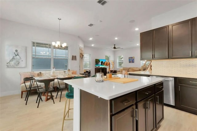 kitchen featuring hanging light fixtures, tasteful backsplash, ceiling fan with notable chandelier, dishwasher, and light wood-type flooring