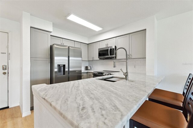 kitchen featuring light hardwood / wood-style flooring, appliances with stainless steel finishes, gray cabinets, tasteful backsplash, and a breakfast bar