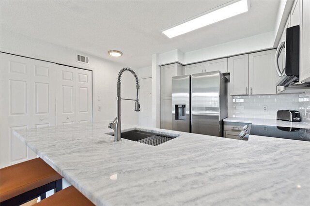 kitchen featuring backsplash, stainless steel appliances, sink, kitchen peninsula, and light stone counters