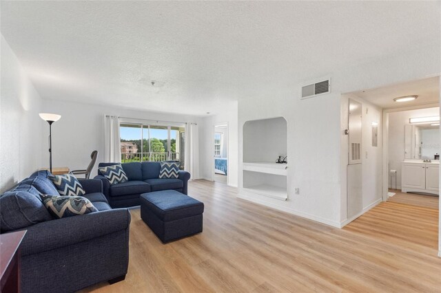 living room with built in features, light hardwood / wood-style floors, and a textured ceiling