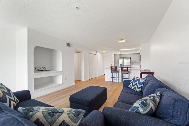 living room featuring a textured ceiling, light hardwood / wood-style flooring, and built in features