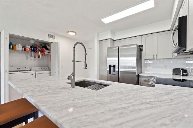 kitchen featuring stainless steel appliances, kitchen peninsula, washing machine and dryer, sink, and decorative backsplash