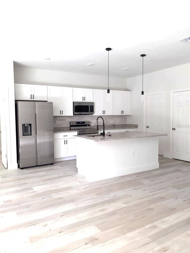 kitchen featuring pendant lighting, light hardwood / wood-style flooring, a kitchen island with sink, stainless steel appliances, and white cabinets