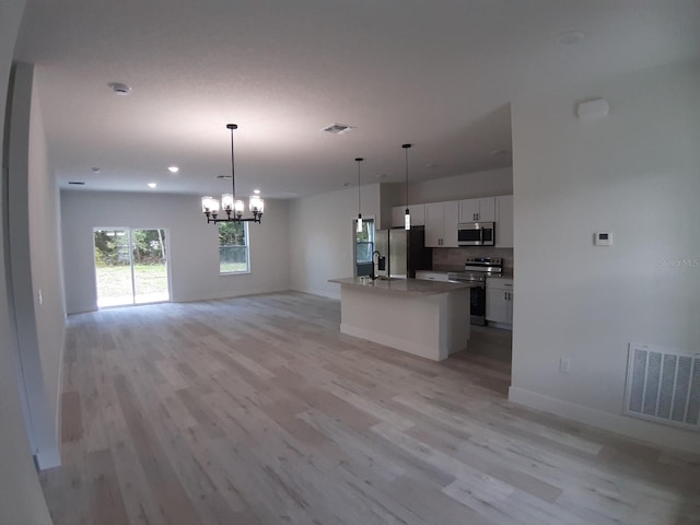 kitchen featuring light hardwood / wood-style flooring, pendant lighting, stainless steel appliances, a kitchen island with sink, and white cabinets