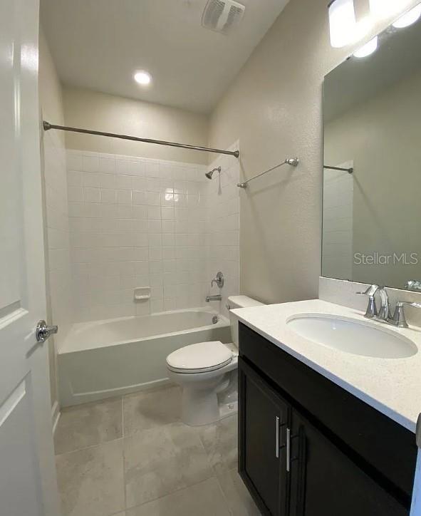 full bathroom with tile patterned flooring, tiled shower / bath, vanity, and toilet