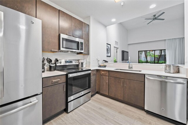 kitchen with sink, ceiling fan, appliances with stainless steel finishes, lofted ceiling, and light hardwood / wood-style floors