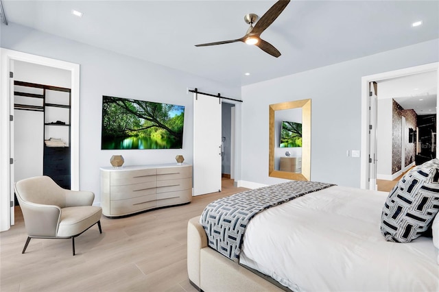 bedroom with ceiling fan, a barn door, a closet, and light hardwood / wood-style flooring