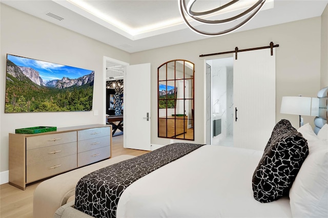 bedroom with ensuite bathroom, a barn door, and light hardwood / wood-style flooring