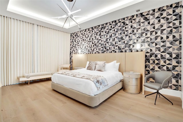 bedroom featuring a raised ceiling, wood-type flooring, and an inviting chandelier