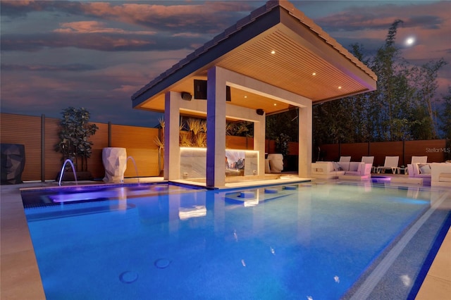 pool at dusk with pool water feature, an in ground hot tub, and a patio