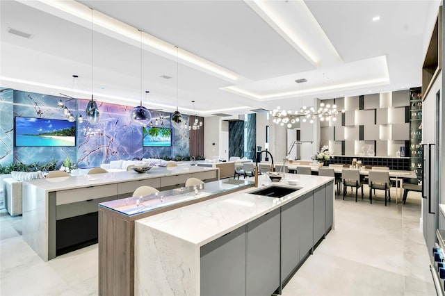 kitchen with a tray ceiling, sink, a spacious island, and decorative light fixtures