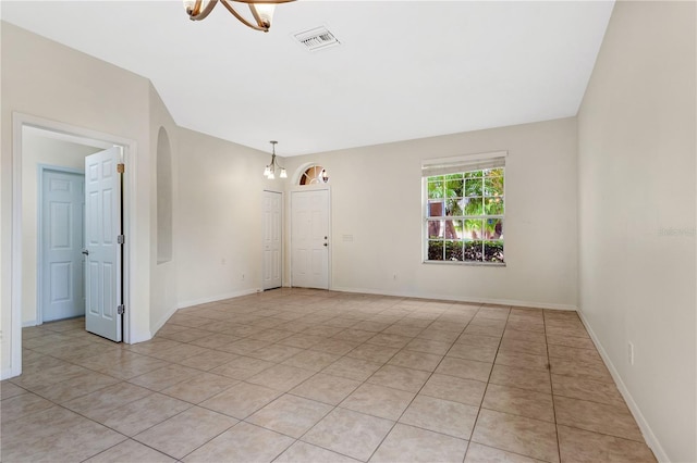 tiled spare room with an inviting chandelier