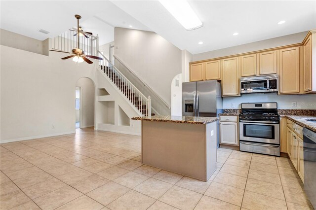 kitchen with a towering ceiling, light tile patterned floors, a kitchen island, and appliances with stainless steel finishes