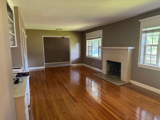 unfurnished living room with a healthy amount of sunlight, a brick fireplace, baseboards, and wood finished floors