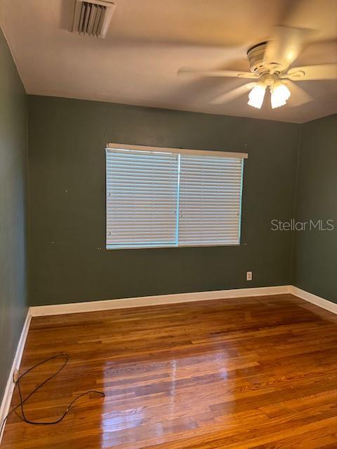 empty room with visible vents, ceiling fan, baseboards, and wood finished floors