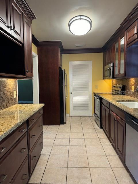 kitchen featuring light tile patterned floors, stainless steel appliances, a sink, glass insert cabinets, and crown molding