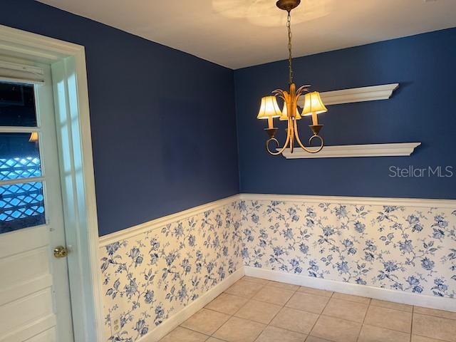 interior space featuring wallpapered walls, tile patterned flooring, an inviting chandelier, and wainscoting