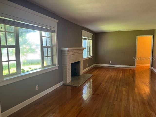 unfurnished living room featuring a brick fireplace, visible vents, baseboards, and wood finished floors